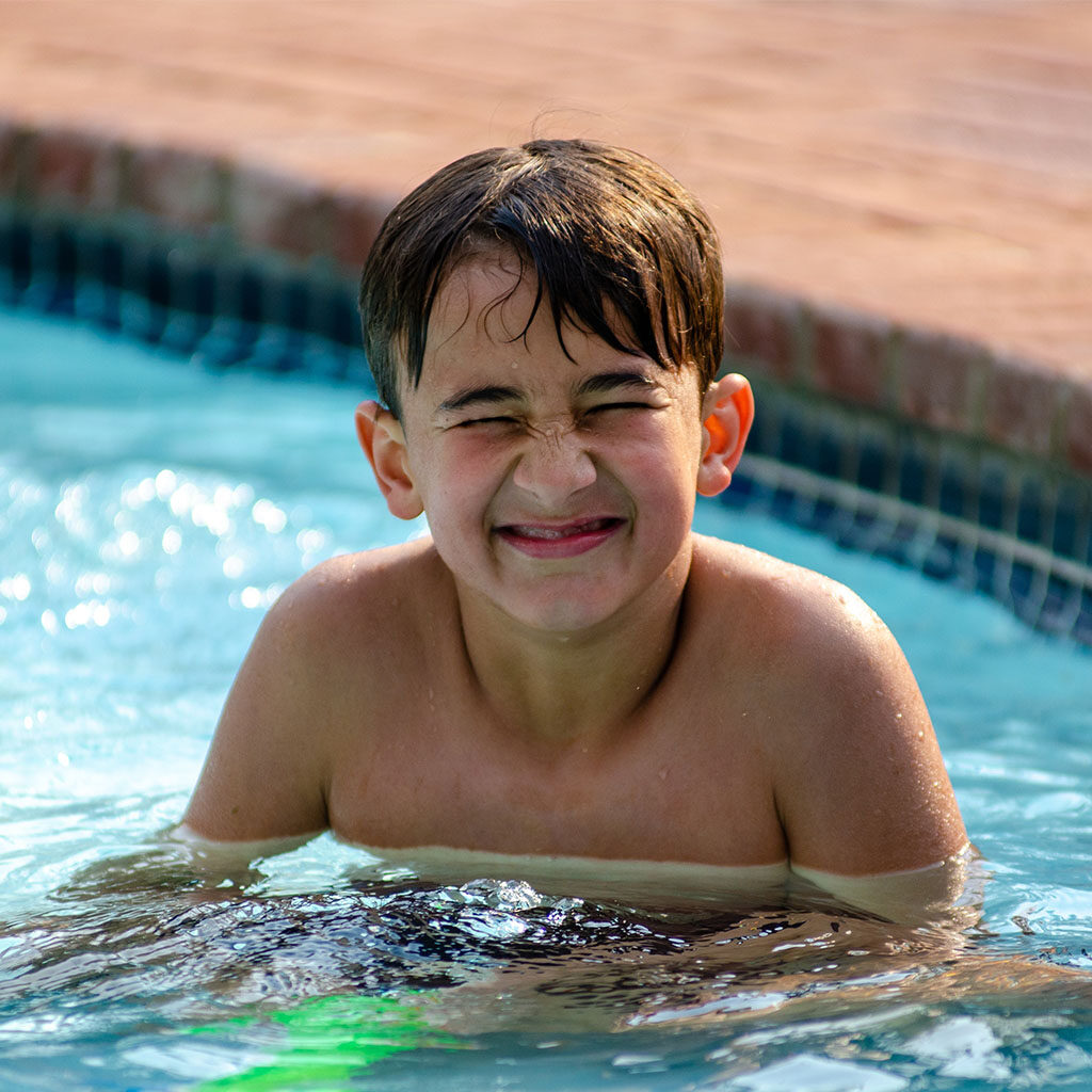 A boy squints in a fiberglass pool. He is happy.